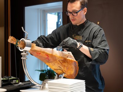 A whole leg of jamón carved to order over a stack of plates