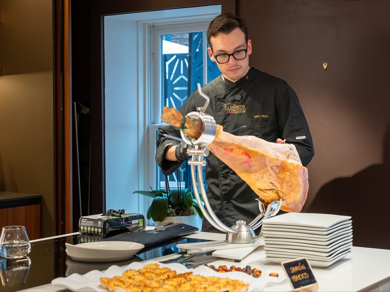 Jamón ibérico being hand-carved on a VETTii kitchen counter, with tapas plated alongside