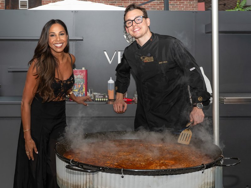 Two of the evening's hosts behind the paella pan as it steams, under the VETTii lettering